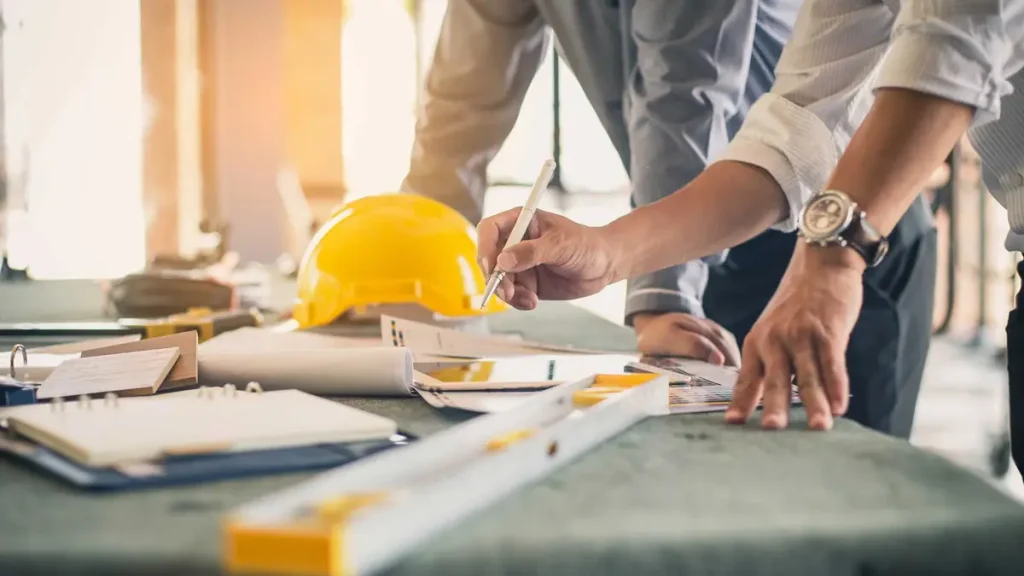Engineers marking up plans next to a yellow hard hat