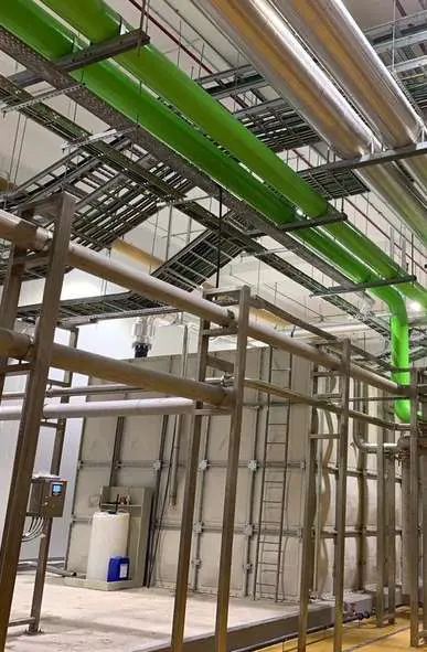 Green pipework and cable trays on steel supports in a plant room