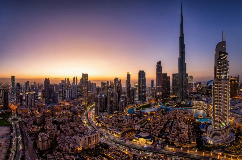 City skyline at dusk with high-rise towers glowing against an orange sky