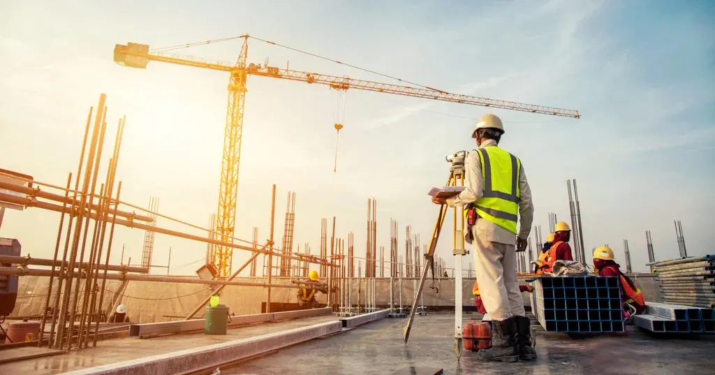 Surveyor in a hard hat on a construction site with a tower crane at sunset